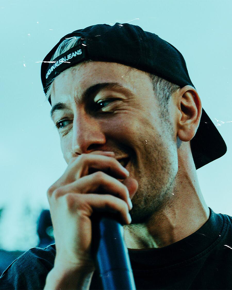 mace, rapper mit mikrofon und cap vor urbaner kulisse