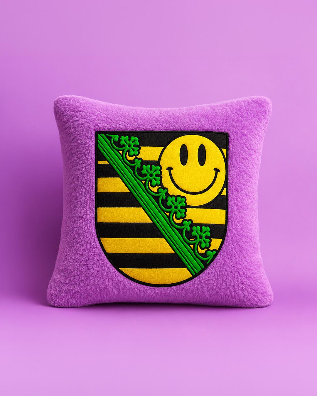 midi x sachsentrance, lila plüschkissen mit sächsischem wappen und gelbem smiley