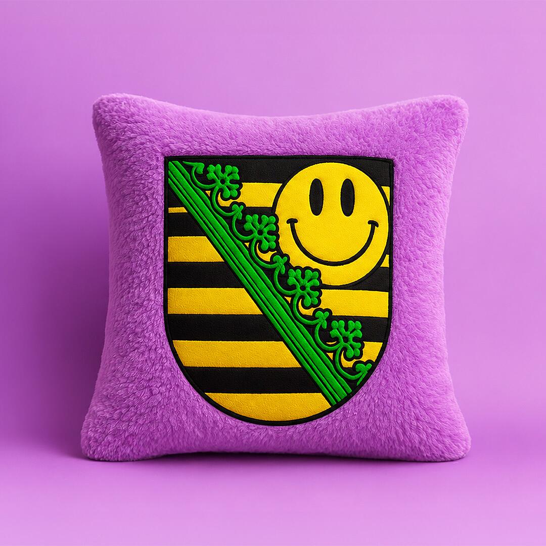 midi x sachsentrance, lila plüschkissen mit sächsischem wappen und gelbem smiley