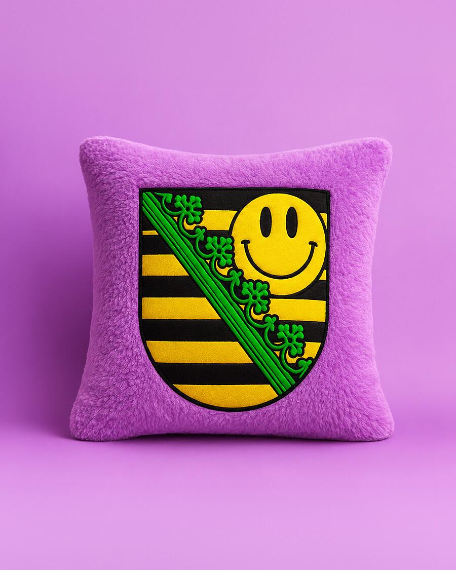 midi x sachsentrance, lila plüschkissen mit sächsischem wappen und gelbem smiley