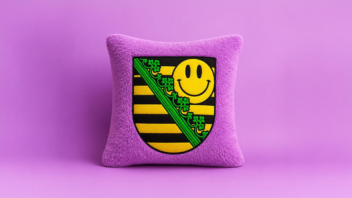 midi x sachsentrance, lila plüschkissen mit sächsischem wappen und gelbem smiley