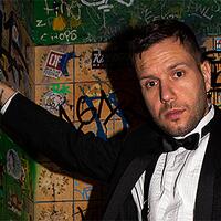 MC Bomber, Mann im Anzug vor Graffitiwand in Toilette